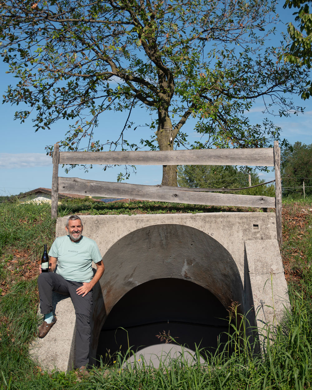 Veduta esterna di unio degli ingressi al bunker storico di Pomerio con Massimo Santinelli appoggiato di fianco mentre tiene in mano una bottiglia di vino Pomerio.